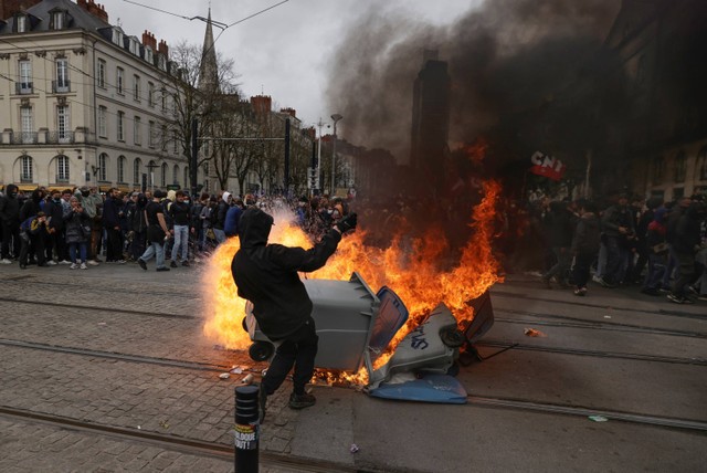 Seorang pengunjuk rasa berdiri di samping wadah limbah yang terbakar saat unjuk rasa di Nantes, Prancis barat. Foto: Jeremias Gonzalez/AP PHOTO