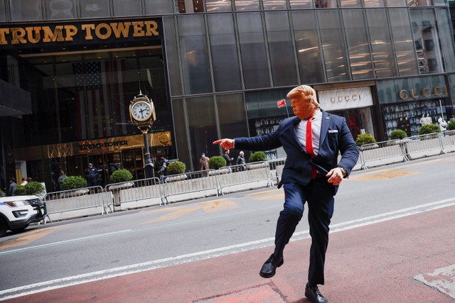 Seseorang yang mengenakan topeng yang menggambarkan mantan Presiden AS Donald Trump memberi isyarat di luar Trump Tower. Foto: Amanda Perobelli/Reuters