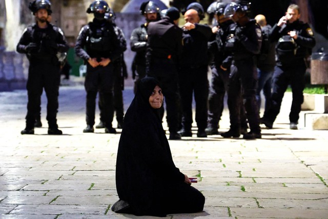 Seorang wanita Palestina duduk di dekat polisi perbatasan Israel di kompleks Masjid Al-Aqsa, Rabu (5/4/2023). Foto: Ammar Awad/REUTERS