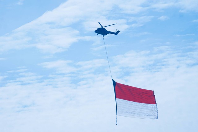 Atraksi helikopter yang membawa bendera Merah Putih raksasa saat peringatan HUT TNI AU ke-77 di Lanud Halim Perdanakusuma, Minggu (9/4). Foto: Iqbal Firdaus/kumparan