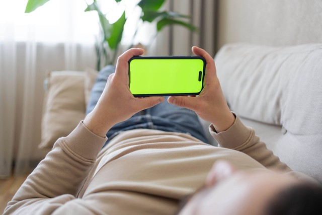 Ilustrasi bermain gadget sambil tiduran. Foto: Julija Sulkovska/Shutterstock