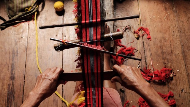 Seorang perempuan menenun dengan alat tradisional.