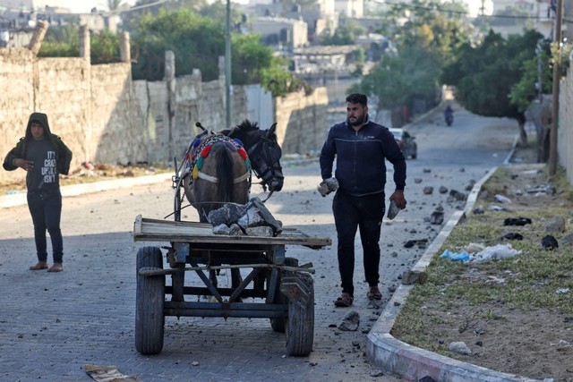 Seorang pria Palestina mengumpulkan puing-puing dari sebuah jalan usai serangan udara dari Israel, di Kota Gaza, Palestina, pada Rabu (3/5/2023). Foto: Mohammed Abed/AFP