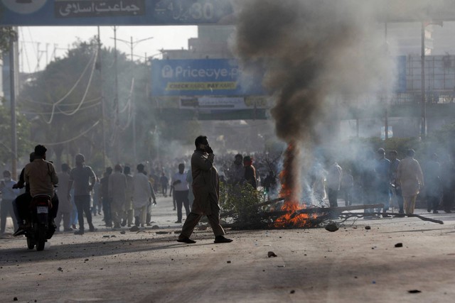 Seorang pria melintasi jalan melewati barikade yang dibakar oleh para pendukung mantan Perdana Menteri Pakistan Imran Khan selama protes terhadap penangkapannya, di Karachi, Pakistan, Selasa (9/10/2023). Foto: Akhtar Soomro/REUTERS