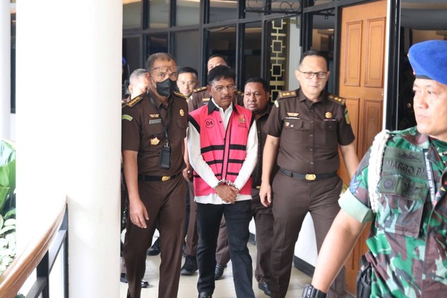Menteri Komunikasi dan Informatika Johnny G Plate (tengah) mengenakan baju tahanan berjalan usai menjalani pemeriksaan di Kejaksaan Agung (Kejagung), Jakarta, Rabu (17/5/2023). Foto: Kejagung