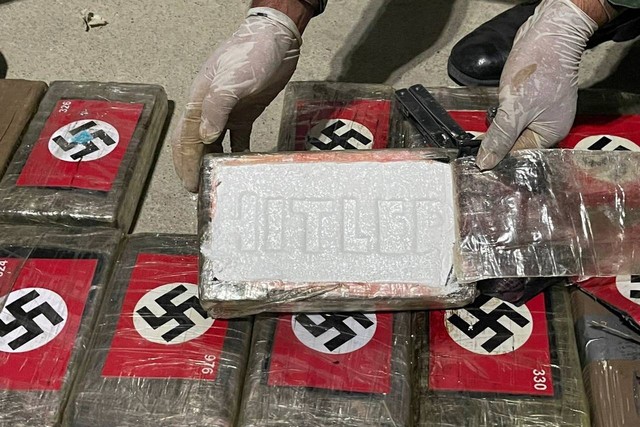 Seorang petugas polisi memegang paket kokain bertanda nama "Hitler", di antara lusinan paket kokain bertanda swastika Nazi, setelah disita oleh polisi Peru di dalam kontainer berpendingin di pelabuhan Paita, Peru, Jumat (26/5/2023). Foto: Peru Police/Handout via REUTERS
