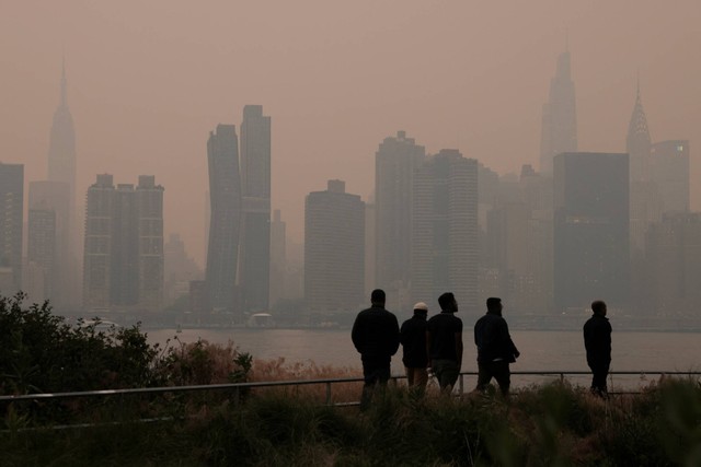 Orang-orang berjalan di tengah kabut dan asap yang disebabkan oleh kebakaran hutan di Kanada yang menutupi cakrawala Manhattan, di New York City, New York, AS, Rabu (7/6/2023). Foto: Andrew Kelly/REUTERS