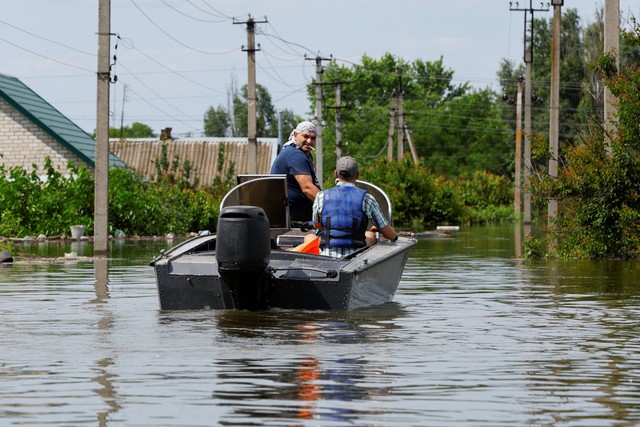 Para pria mengarungi perahu motor di daerah pemukiman yang tergenang air, yang terendam air setelah runtuhnya bendungan Nova Kakhovka, di Kherson, Ukraina, Rabu (7/6/2023). Foto: Alexander Ermochenko/REUTERS