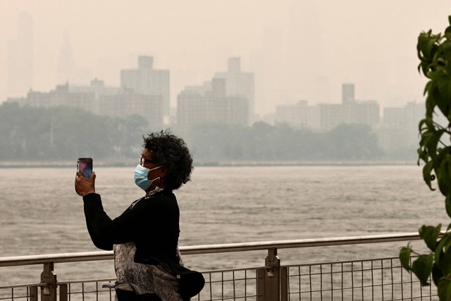 Seseorang yang memakai masker mengambil gambar cakrawala Manhattan yang tertutup kabut dan asap akibat kebakaran hutan di Kanada, di Brooklyn, New York, Amerika Serikat, Rabu (7/6/2023). Foto: Amr Alfiky/REUTERS