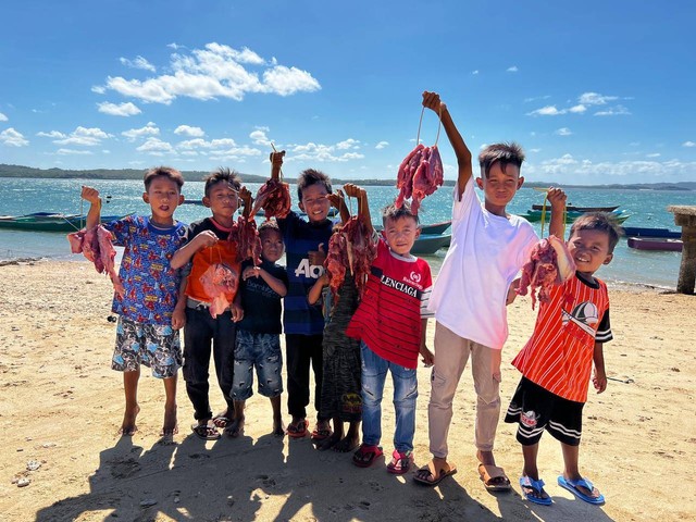 Anak-anak di Rote NTT bersuka cita setelah mendapat potongan daging kurban saat Idul Adha 2022. Pemotongan daging kurban dilakukan di pantai sekitar pemukiman mereka.