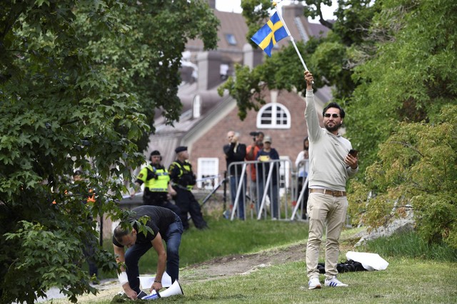 Pengunjuk rasa Salwan Momika mengibarkan bendera Swedia di luar kedutaan Irak di Stockholm, Swedia, untuk membakar salinan Al-quran dan bendera Irak, Kamis (20/7/2023). Foto: Oscar Olsson/TT via AP