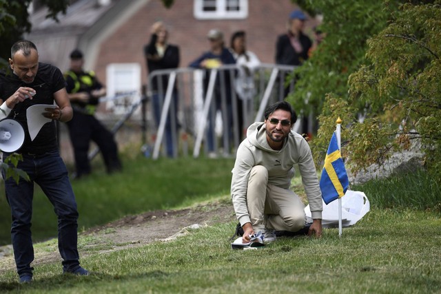Pengunjuk rasa Salwan Momika berlutut di samping bendera Swedia di luar kedutaan Irak di Stockholm, Swedia, untuk membakar salinan Al-quran dan bendera Irak, Kamis (20/7/2023).
