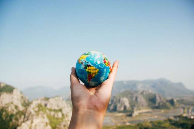 person holding world globe facing mountain. Sumber Ilustrasi : www.pexels.com