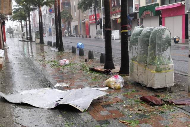 Puing-puing berserakan di jalan pusat kota saat angin kencang akibat Topan Khanun menghantam kota Naha, prefektur Okinawa pada Selasa (2/8/2023). Foto: STR/JIJI Press/AFP