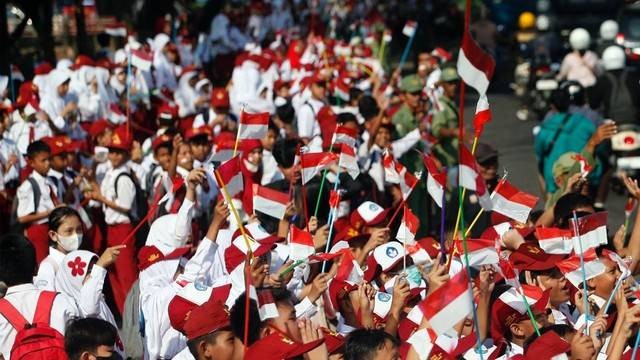 Sejumlah siswa Sekolah Dasar (SD) mengibarkan bendera merah putih di pinggir Jalan Raya Bogor, Cibinong, Kabupaten Bogor, Jawa Barat. Foto: ANTARA FOTO/Yulius Satria Wijaya