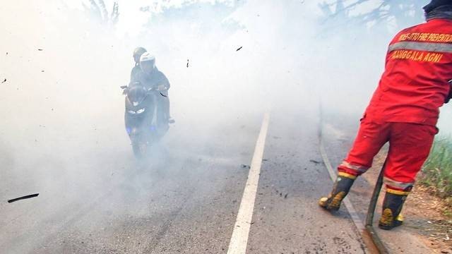 Pengendara motor yang menerobos kepulan asap yang berasal dari kebakaran lahan dan hutan di jalur lintas Sumatera, Ogan Ilir, Sumsel, Minggu (3/9) Foto: ary priyanto/urban id