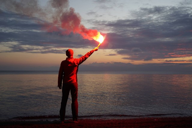 Ilustrasi pria menyalakan flare di pantai sebagai tanda SOS atau sinyal membutuhkan pertolongan. Foto: StockVisual/Shutterstock