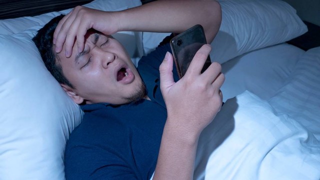 Ilustrasi pria main handphone sebelum tidur. Foto: airdone/Shutterstock