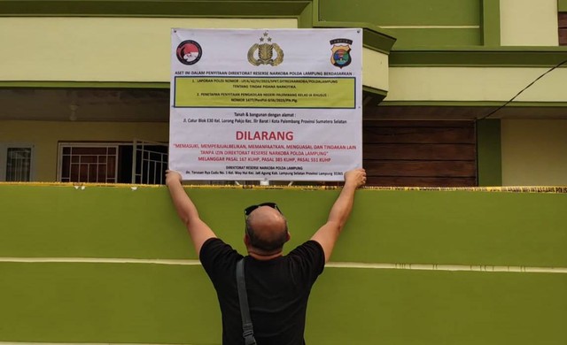 Petugas polisi saat memasang plang penyitaan aset milik istri bandar narkoba di Palembang. (ist)
