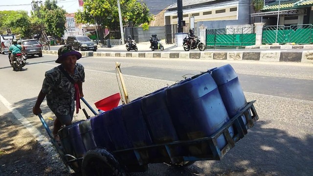 Potret Hadi dorong gerobak berisi pesanan air bersih dalam jeriken. (Pribadi/Rifki)