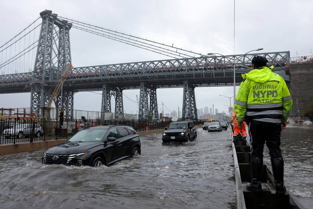 Seorang petugas polisi dari Patroli Jalan Raya NYPD mengamati pengendara yang berkendara melalui jalan yang banjir di Manhattan dekat jembatan Williamsburg, di New York City, AS, Jumat (29/9/2023). Foto: Andrew Kelly/REUTERS