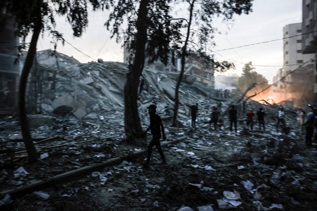 Warga berjalan di dekat reruntuhan menara yang hancur akibat serangan udara Israel di Kota Gaza, Sabtu (7/10/2023).  Foto: Mohammed ABED / AFP