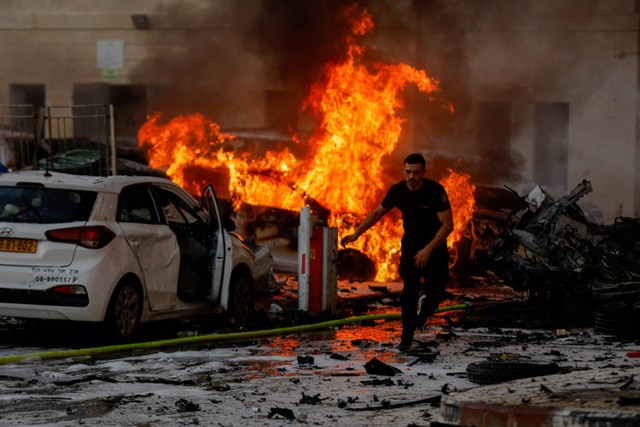 Seorang pria berlari di jalan saat api berkobar setelah roket diluncurkan dari Jalur Gaza, di Ashkelon, Israel, Sabtu (7/10/2023).  Foto: Amir Cohen/REUTERS