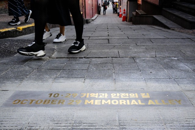 Pejalan kaki berjalan melewati tulisan yang baru diresmikan bertuliskan 29 Oktober Memorial Alley di Itaewon, Seoul, Korea Selatan, Rabu (25/10/2023). Foto: Anthony Wallace/AFP