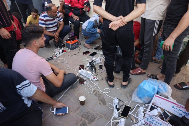 Pria Palestina mengisi daya ponsel mereka di titik listrik kolektif di tempat penampungan di Khan Younis di Jalur Gaza selatan, pada Kamis (26/10//2023). Foto: Mohammed Abed/AFP