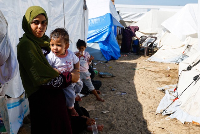 Seorang wanita menggendong anak di lokasi pengungsian di tengah serangan Israel, berlindung di tenda kamp di pusat yang dikelola PBB, di Khan Younis di selatan Jalur Gaza, 30 Oktober 2023.  Foto: REUTERS/Ibraheem Abu Mustafa