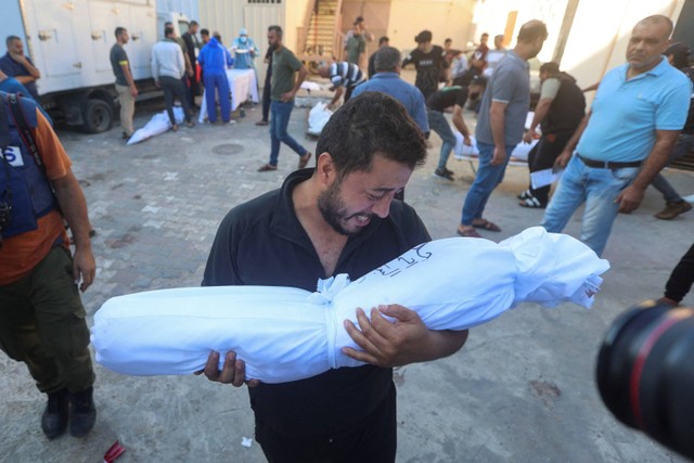 Seorang pria Palestina membawa jenazah seorang anak yang tewas dalam serangan Israel, di rumah sakit Shuhada Al-Aqsa di Jalur Gaza tengah 31 Oktober 2023. Foto: Ahmed Zakot/Reuters