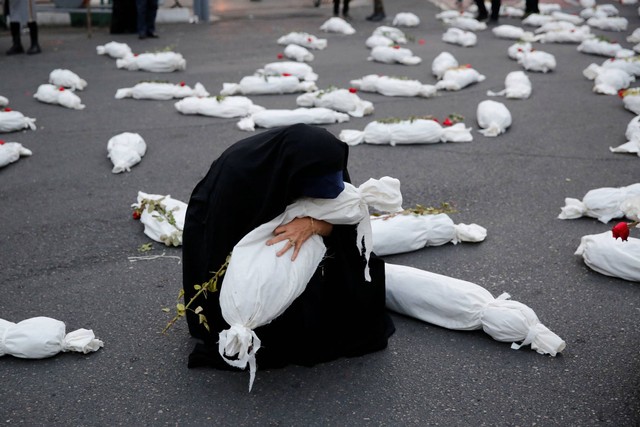 Seorang wanita memeluk instalasi yang menampilkan simbolis mayat anak-anak Gaza di alun-alun Palestina di Kota Teheran, Iran, pada Senin (13/11/2023). Foto: Atta Kenare/AFP