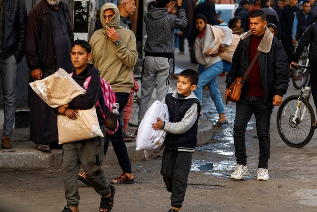 Anak-anak Palestina yang terlantar membawa barang-barang saat mereka hendak pulang, selama gencatan senjata sementara antara Hamas dan Israel, di Khan Younis di selatan Jalur Gaza, Jumat (24/11/2023). Foto: Ibraheem Abu Mustafa/REUTERS