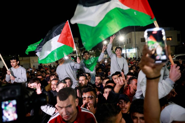 Tahanan Palestina yang dibebaskan mengibarkan bendera saat mereka meninggalkan penjara militer Israel, Ofer, di dekat Ramallah di Tepi Barat yang diduduki Israel, Jumat (24/11/2023). Foto: Ammar Awad/REUTERS