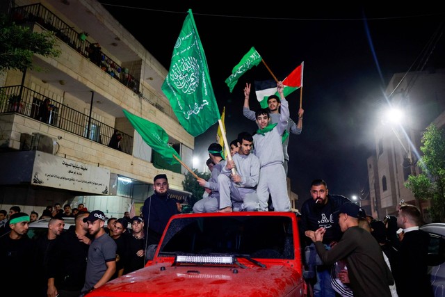 Tahanan Palestina yang dibebaskan mengibarkan bendera saat mereka meninggalkan penjara militer Israel, Ofer, di dekat Ramallah di Tepi Barat yang diduduki Israel, Jumat (24/11/2023). Foto: Ammar Awad/REUTERS