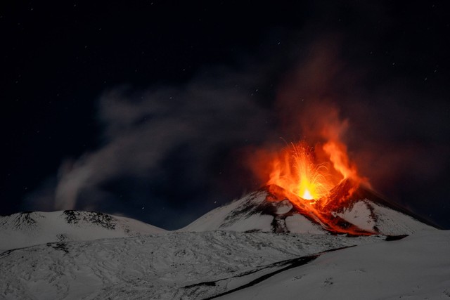 Gumpalan asap dan lava membubung dari salju yang menutupi Gunung Etna terlihat dari Monte San Leo, Italia, Jumat (24/11/2023). Foto: Etna Walk/Oleh Giuseppe Di Stefano/HO via REUTERS