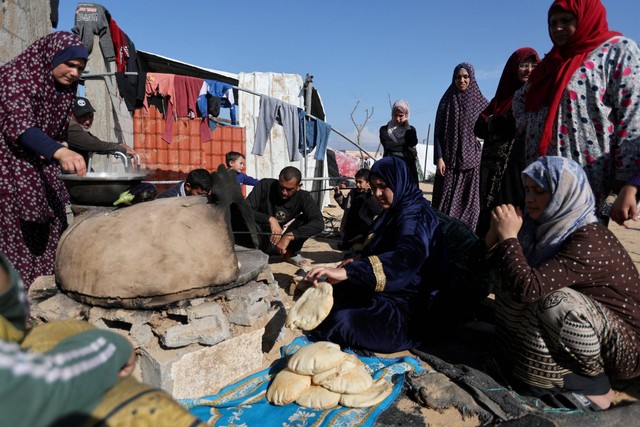 Orang-orang menunggu sementara seorang wanita menyiapkan makanan, di sebuah kamp di Rafah, di Jalur Gaza selatan, Rabu (6/12/2023). Foto: Ibraheem Abu Mustafa/REUTERS