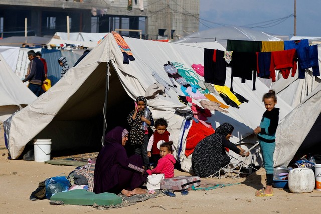 Seorang wanita duduk bersama anak-anak di luar, saat warga Palestina berlindung di sebuah kamp di Rafah, di Jalur Gaza selatan, Rabu (6/12/2023). Foto: Ibraheem Abu Mustafa/REUTERS