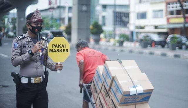 Seorang anggota kepolisian yang tengah mensosialisasikan pemakaian masker di Jalan Sudirman Palembang, Rabu (16/9) Foto: ary priyanto/Urban Id