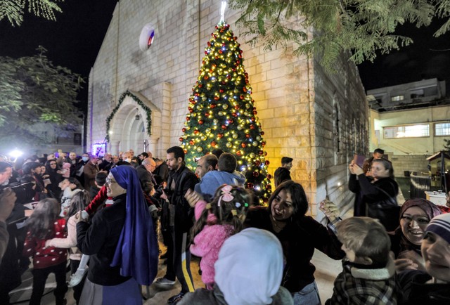 Masyarakat berkumpul saat menghadiri perayaan penyalaan pohon Natal di Gereja Katolik Roma Keluarga Kudus di Kota Gaza pada 18 Desember 2021. Foto: MAHMUD HAMS / AFP