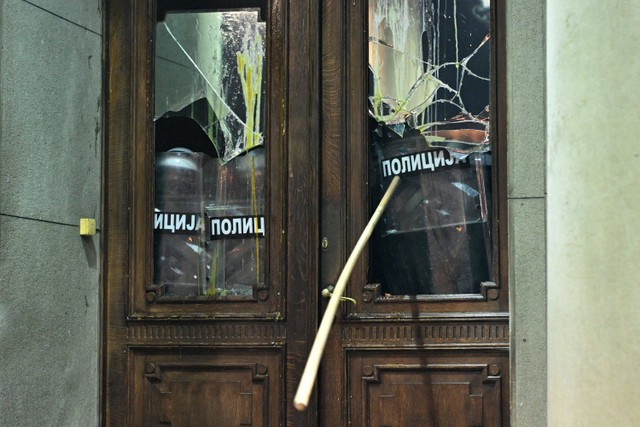 Seorang pengunjuk rasa merusak pintu masuk gedung dewan kota Beograd selama demonstrasi di Beograd, Serbia, Minggu (24/12/2023). Foto: OLIVER BUNIC / AFP