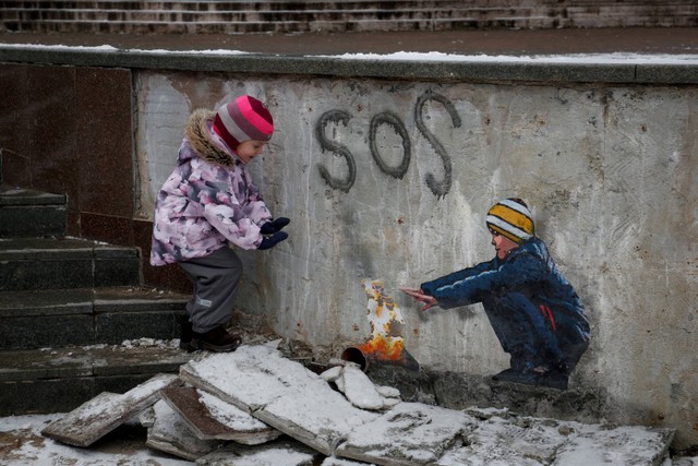 Seorang anak berdiri di samping karya seni seniman jalanan terkenal Tvboy di pusat kota Bucha, Ukraina pada 29 Januari 2023. Foto: Valentyn Ogirenko/REUTERS