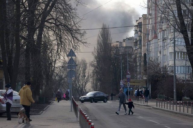 Seorang wanita dengan seorang anak menyeberang jalan, sementara asap mengepul dari api setelah serangan roket di pusat kota Kiev, Ukraina, pada Jumat (29/12/2023). Foto: Anatolii Stepanov/AFP