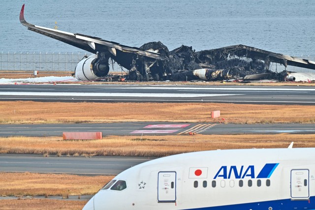 Pesawat All Nippon Airlines (ANA) melewati puing-puing pesawat penumpang Japan Airlines (JAL) yang terbakar di landasan Bandara Internasional Haneda di Tokyo, Jepang, Rabu (3/1/2024). Foto: Richard A. Brooks/AFP