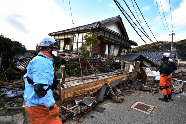 Petugas pemadam kebakaran memeriksa rumah-rumah kayu yang runtuh di Wajima, prefektur Ishikawa, Jepang pada Selasa (2/1/2024). Foto: Kazuhiro Nogi/AFP