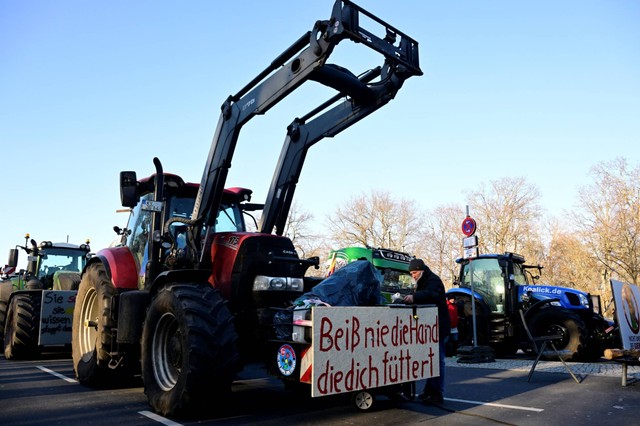 Sebuah plakat bertuliskan 'Jangan gigit tangan yang memberi makan Anda' dipasang pada traktor yang diparkir di jalan raya "Strasse des 17 Juni", menuju Gerbang Brandenburg di Berlin, Jerman, Senin (8/1/2024). Foto: John Macdougall/AFP