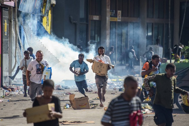 Warga berlarian membawa membawa barang-barang rampasan di tengah kerusuhan di Port Moresby, Papua Nugini, Rabu (10/1/2024). Foto: Andrew KUTAN / AFP