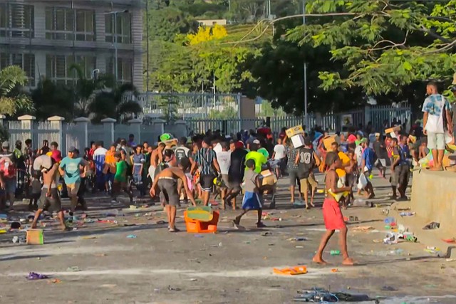 Warga berlarian membawa membawa barang-barang rampasan di tengah kerusuhan di Port Moresby, Papua Nugini, Rabu (10/1/2024). Foto: STR/AFP