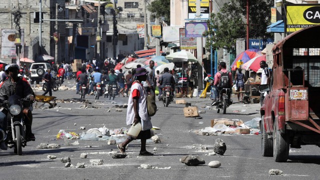 Orang-orang berjalan dan berkendara di jalan yang tertutup puing-puing dan batu yang digunakan untuk memblokir jalan, sementara barikade yang terbakar di beberapa lingkungan memaksa warga untuk berlindung, di Port-au-Prince, 
Haiti 18 Januari 2024. Foto: REUTERS/Ralph Tedy Erol