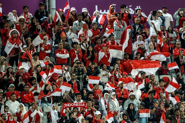 Suporter Indonesia memegang plakat saat suporter Qatar Indonesia bersorak saat pertandingan sepak bola Grup D Piala Asia AFC Qatar 2023 antara Vietnam dan Indonesia di Stadion Abdullah bin Khalifa di Doha, Qatar, Jumat (19/1/2024). Foto: Karim Jaafar/AFP